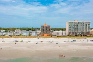 Ein Strand mit einer Reihe von Gebäuden, darunter ein Hotel und Wohnhäuser.