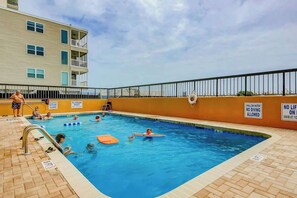A swimming pool area with a lifeguard stand, poolside chairs, and a building with balconies in the background. - Wellington Unit 304 Condo (North Myrtle Beach)