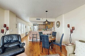 A spacious living area with a dining table, leather chairs, and a kitchen in the background. - Wellington Unit 304 Condo (North Myrtle Beach)