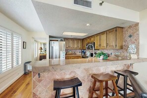 A kitchen with a central island, wooden cabinets, and a stone backsplash. - Wellington Unit 304 Condo (North Myrtle Beach)