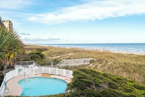 A pool with a view of the beach and ocean, surrounded by a white fence and greenery. - Salty Mermaid at Wind Crest Villas (North Myrtle Beach)