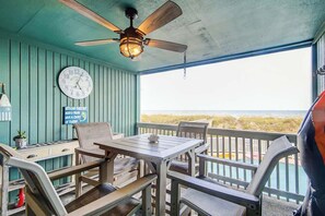 A covered outdoor seating area with a table and chairs, a ceiling fan, a clock, and a view of the beach. - Salty Mermaid at Wind Crest Villas (North Myrtle Beach)