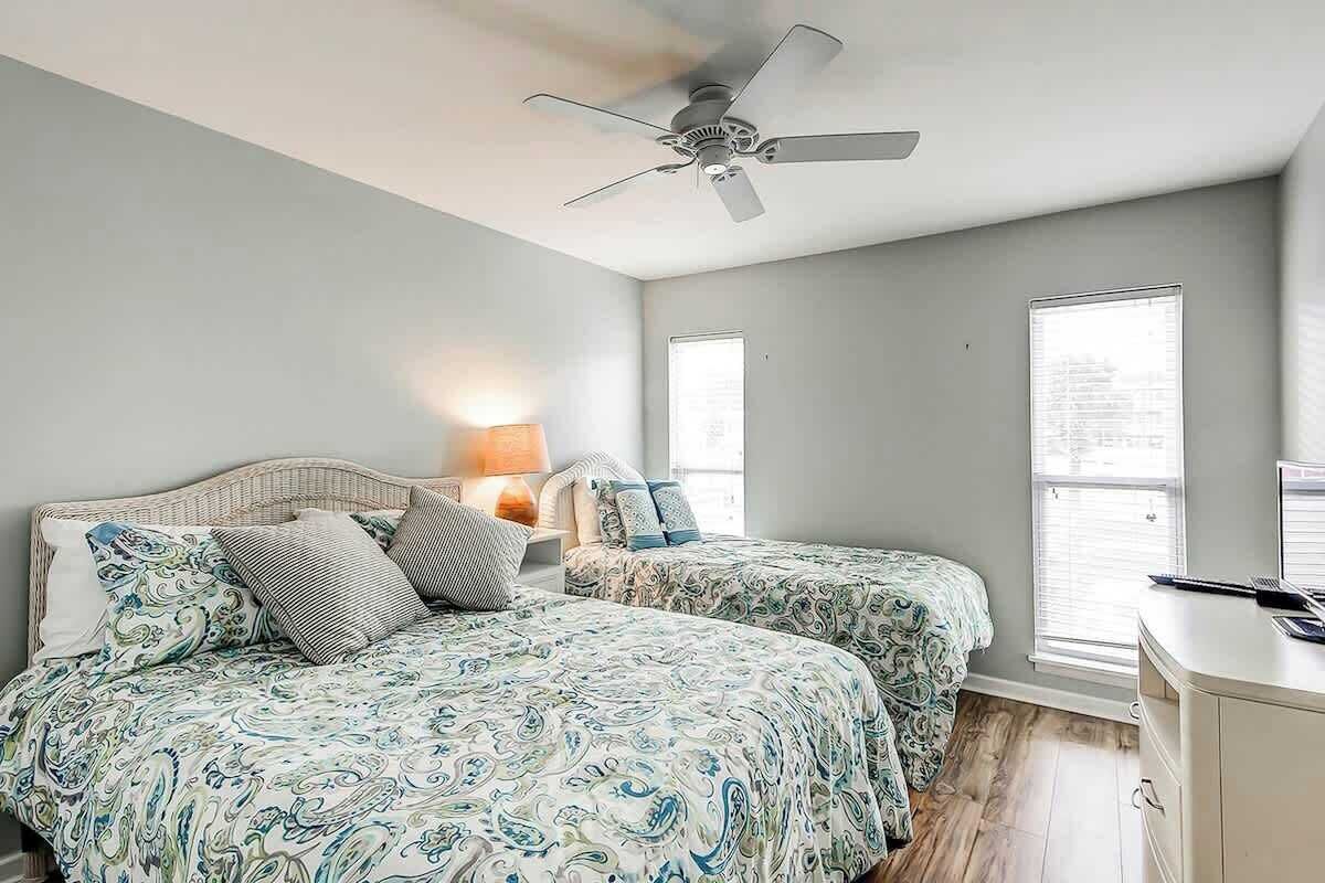 A bedroom with two beds, a ceiling fan, a nightstand with a lamp, and a dresser.