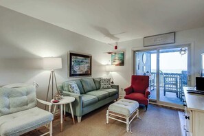 Un salon avec un canapé, un fauteuil et une chaise rouge. On y trouve une table avec une lampe, ainsi qu’un tableau accroché au mur.