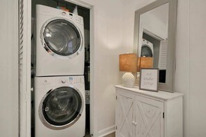 A laundry room with two stacked front-loading washing machines, a cabinet with a mirror, and a 'no wake zone' sign. - Lovely Beach Bungalow (North Myrtle Beach)