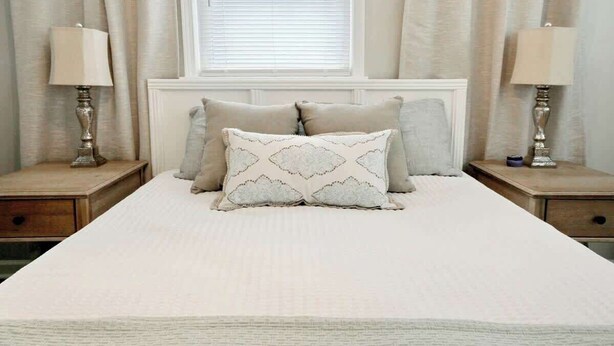 Un dormitorio con una cama grande, dos mesitas de noche y un ventanal con cortinas.