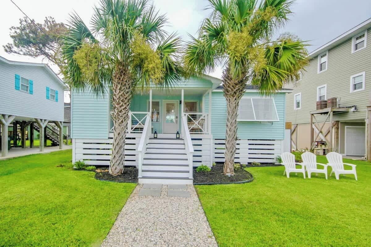 A two-story house with a porch, palm trees, and a gravel pathway leading to the entrance.