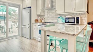 Una cocina moderna con armarios blancos, un refrigerador de acero inoxidable, un microondas y una isla grande con taburetes de bar.