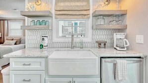 Una cocina con pileta integrada, muebles blancos, ventana con vistas y cafetera.