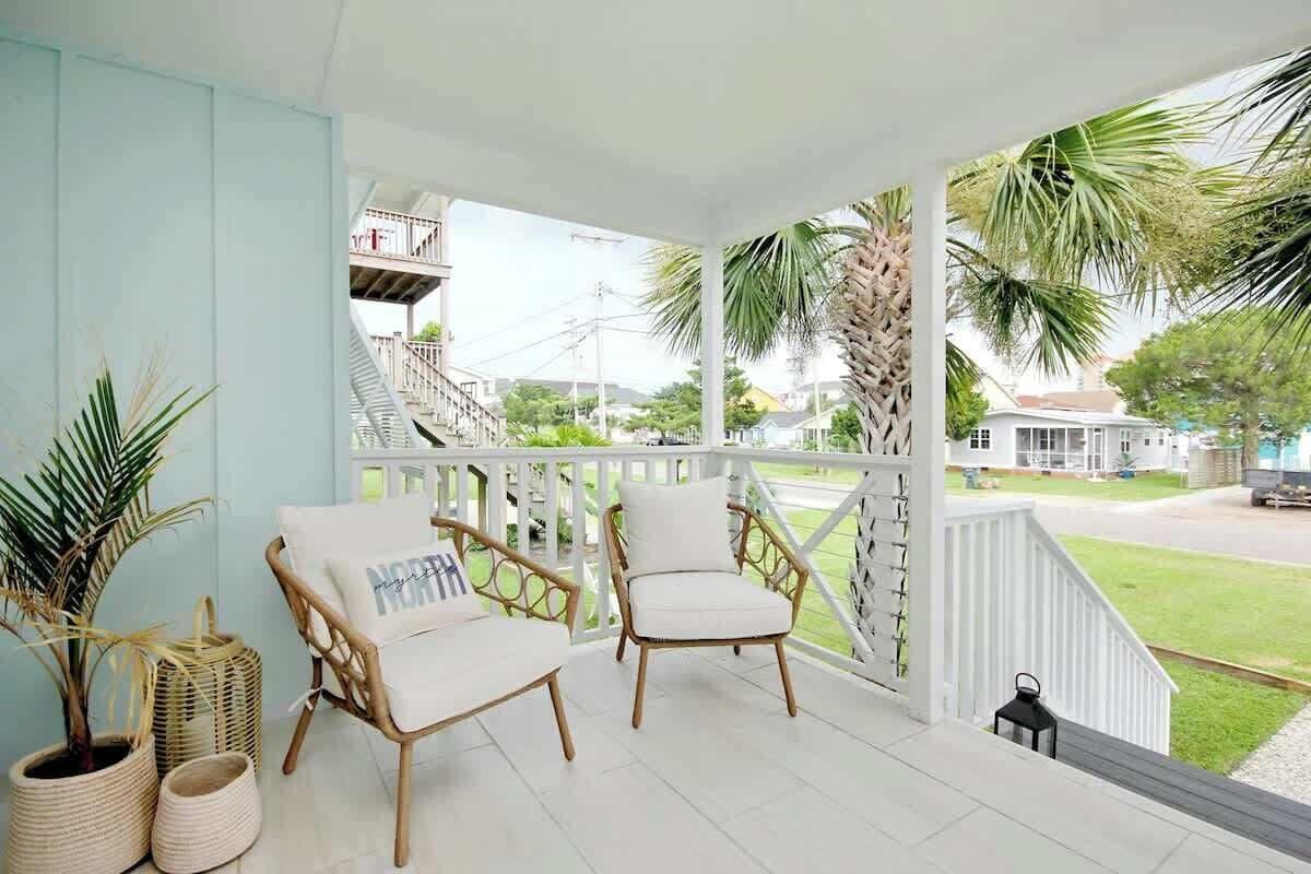 A covered porch with wicker chairs and a view of a residential street.