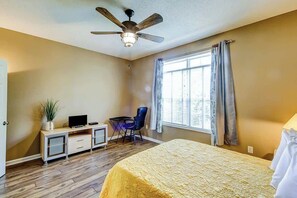Ein Hotelzimmer mit Bett, Schreibtisch mit Stuhl, Deckenventilator und einem Fenster mit Vorhängen.