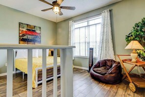 A bedroom with a bed, a ceiling fan, a window with curtains, a radiator, a plant, and a bedside table. - Albatross Beach Retreat (Little River)