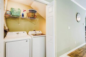 A laundry room with two white washers and dryers, a shelf with cleaning supplies, and a clock on the wall. - Albatross Beach Retreat (Little River)