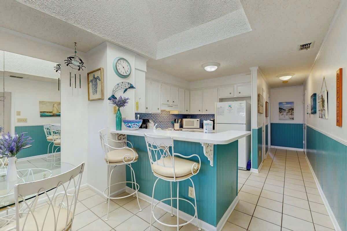 Une cuisine moderne avec des meubles blancs, un îlot central doté de tabourets de bar et un coin repas avec une table et des chaises en verre.
