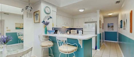 A modern kitchen with white cabinets, a central island with bar stools, and a dining area with a glass table and chairs.