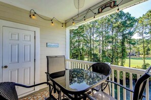 A covered porch with a glass table and chairs, a white door, and a sign reading 'LIFE'S BEACH'. - Golf Retreat Unit 832 (North Myrtle Beach)