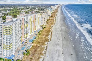 Un quartier résidentiel situé sur la côte, avec de grands immeubles, une plage et un complexe de piscines.