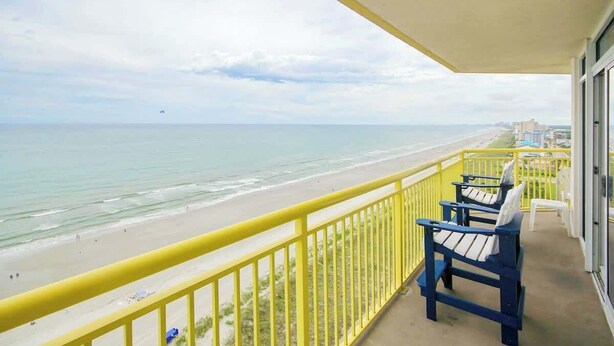 A balcony with a view of the beach and ocean, featuring a yellow railing and blue chairs. - Bay Watch Resort 1740 (North Myrtle Beach)