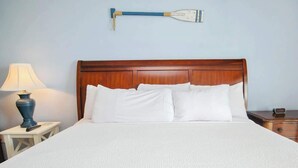 A neatly made bed with white linens, a wooden headboard, a bedside lamp, and a wall-mounted paddleboard. - Bay Watch Resort 1740 (North Myrtle Beach)