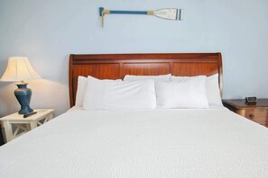 A neatly made bed with white linens, a wooden headboard, a bedside lamp, and a wall-mounted paddleboard. - Bay Watch Resort 1740 (North Myrtle Beach)