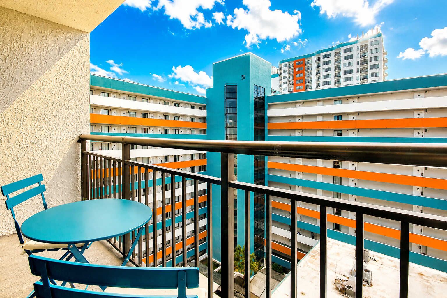 A balcony with a table and chairs, overlooking a multi-story building with orange and white balconies.