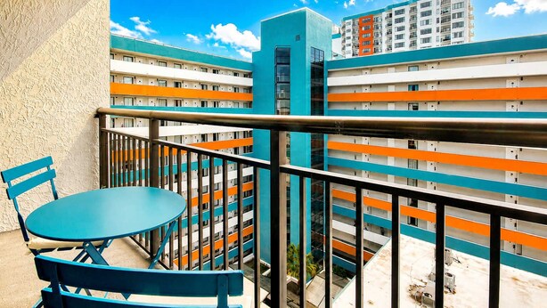A balcony with a table and chairs, overlooking a multi-story building with orange and white balconies. - Landmark Resort 1208 (Myrtle Beach)