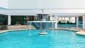 A swimming pool with a central fountain, surrounded by a tiled deck and steps leading to a covered area. - Landmark Resort 1208 (Myrtle Beach)