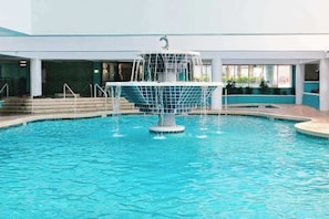 A swimming pool with a central fountain, surrounded by a tiled deck and steps leading to a covered area. - Landmark Resort 1208 (Myrtle Beach)