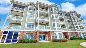 A multi-story residential building with balconies, brick facade, and a clear sky. - Luster Leaf Unit 201 (Myrtle Beach)