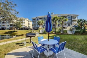Une terrasse avec une table ronde et des chaises bleues, un barbecue et un bassin dans la cour d’un hôtel.
