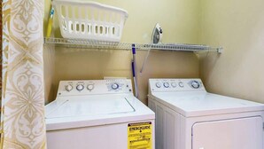 A laundry area with two washing machines, a white basket on a shelf, and a wall-mounted iron. - Luster Leaf Unit 201 (Myrtle Beach)