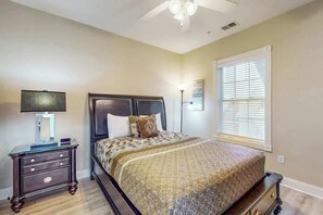 A bedroom with a bed, nightstand, lamp, ceiling fan, and window with blinds. - Luster Leaf Unit 201 (Myrtle Beach)