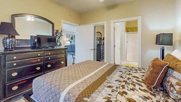 A bedroom with a bed, dresser, mirror, and ceiling fan. - Luster Leaf Unit 201 (Myrtle Beach)