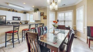 A modern kitchen with white cabinets, a microwave, and a dining area with a glass table and leather chairs. - Luster Leaf Unit 201 (Myrtle Beach)