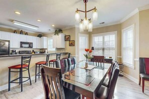 A modern kitchen with white cabinets, a microwave, and a dining area with a glass table and leather chairs.