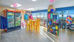 Um espaço interno bem iluminado, com área de estar, um refrigerador de bebidas e diversos itens coloridos nas prateleiras.