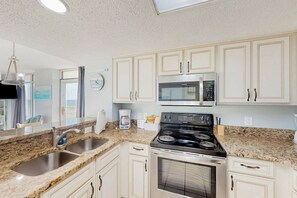 A kitchen with white cabinets, a granite countertop, a stainless steel stove, and a microwave. - Bay Watch Resort 0640 (North Myrtle Beach)