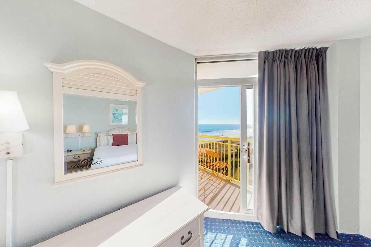 Habitación de hotel con balcón, cama, cómoda y ventana con cortinas.