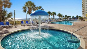 A pool area with a water feature, lounge chairs, and palm trees. - Bay Watch Resort 1741 (North Myrtle Beach)