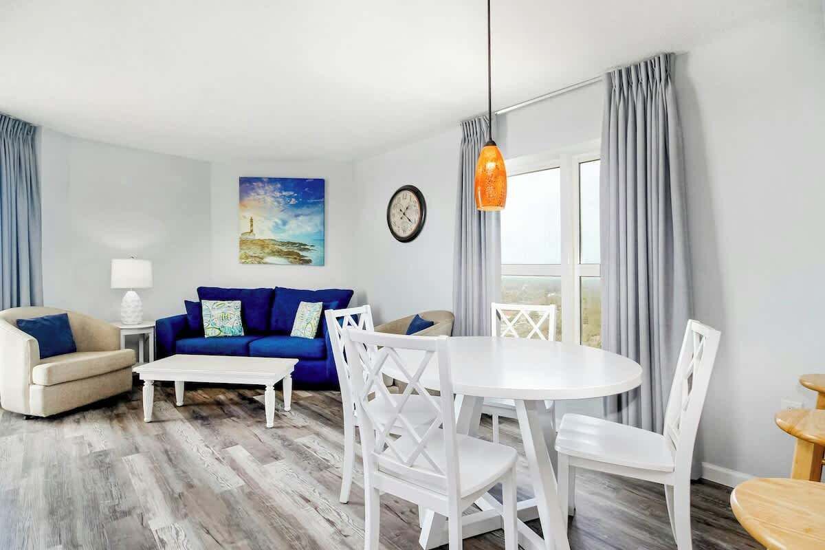 A living room with a blue sofa, white chairs, a round table, and a painting on the wall.