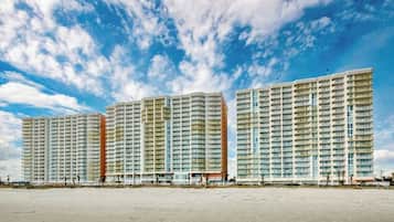 Three high-rise residential buildings with multiple balconies, situated on a flat terrain.