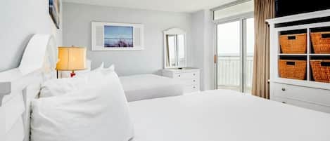 A hotel room with a large bed, a bedside table with a lamp, a dresser, a mirror, and a window with curtains.