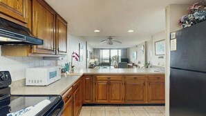 Una cocina con armarios de madera, microondas, refrigerador y ventilador de techo.