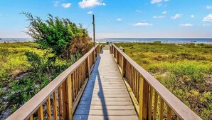Una pasarela de madera que lleva a una playa, con cielo despejado y vista distante del océano.