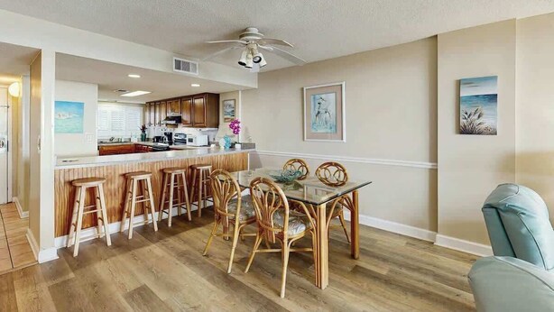 Una cocina moderna con armarios de madera, una isla central con taburetes y un comedor con mesa de vidrio y sillas de mimbre.