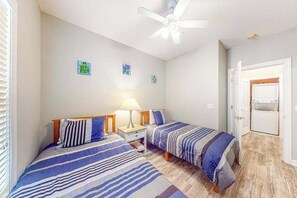 Ein Schlafzimmer mit zwei Betten, einem Deckenventilator und einer Tür zu einem Badezimmer.