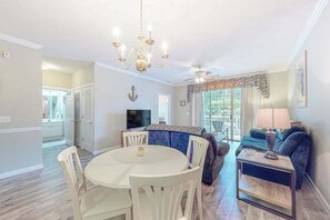 Ein Essbereich mit einem runden Tisch, Stühlen, einer Chandelüster und einem Fernseher im Hintergrund.