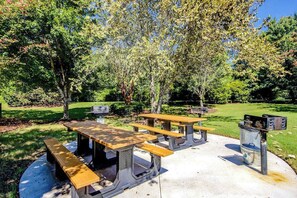 Een picknickplaats buiten met meerdere tafels en banken, omgeven door bomen en gras.