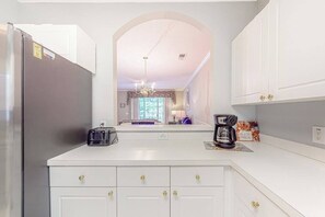 A kitchen with white cabinetry, a refrigerator, a toaster, and a coffee maker. - Barefoot Memories Retreat (North Myrtle Beach)