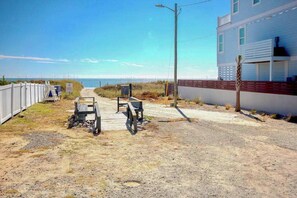 A coastal road leading to a building with a sandy path, benches, and a wooden fence. - Grace by the Sea Retreat (Atlantic Beach)